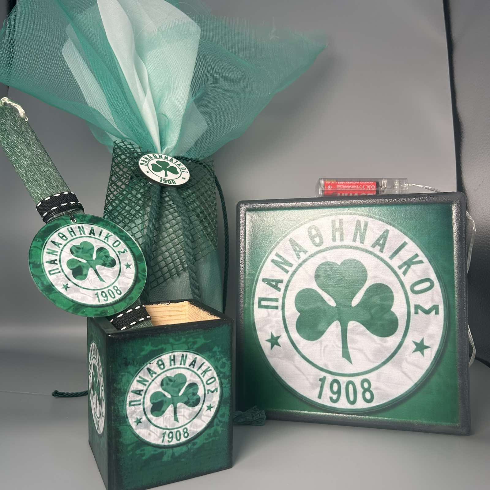 Πράσινη λαμπάδα με το έμβλημα του Παναθηναϊκού, συνοδευόμενη από φωτιζόμενο καδράκι και μολυβοθήκη. Όλα τα αντικείμενα διατίθενται και ξεχωριστά. Πράσινη λαμπάδα με το έμβλημα του Παναθηναϊκού, συνοδευόμενη από φωτιζόμενο καδράκι και μολυβοθήκη. Όλα τα αντικείμενα διατίθενται και ξεχωριστά.